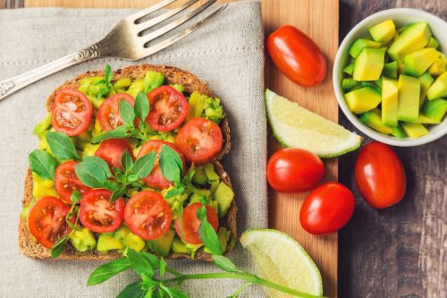Toast with avocado, tomatoes and basil on rustic wooden background