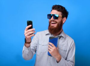 Young Bearded Hipster Man Taking A Selfie With His Cup Of Coffee On Pink Background.